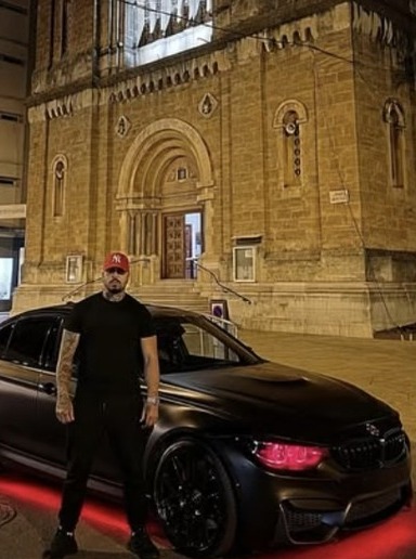 Un homme devant la M3 F80 noire garée devant une église, de nuit